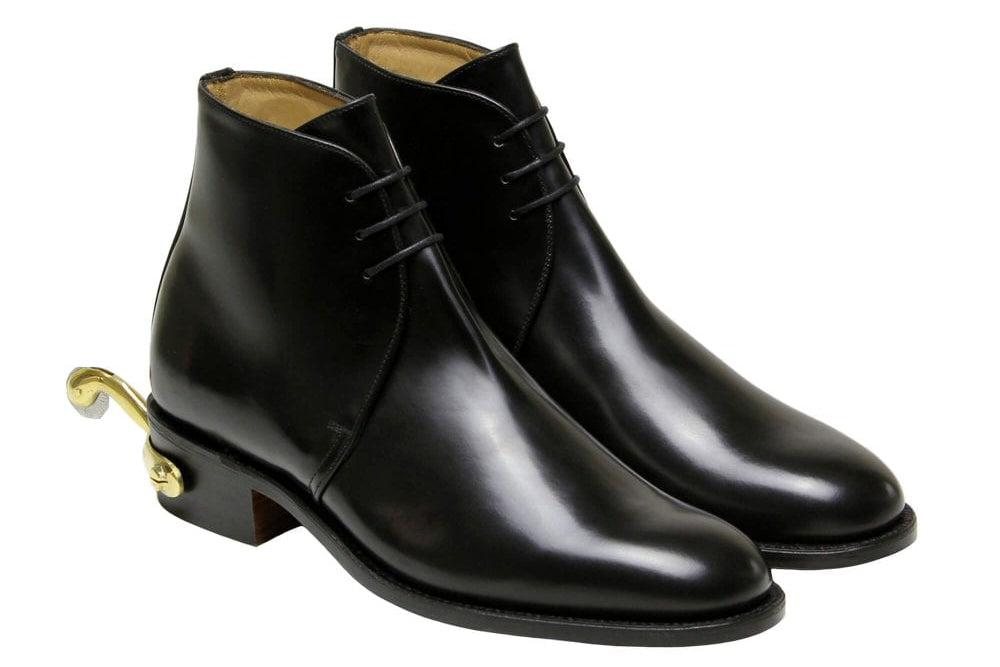 A pair of black leather lace-up ankle boots with a distinctive gold metal hook heel, shown against a plain white background.